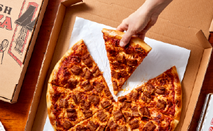 carboard pizza box sitting on a table in a college dorm with hand reaching into it to grab a slice of sausage pizza